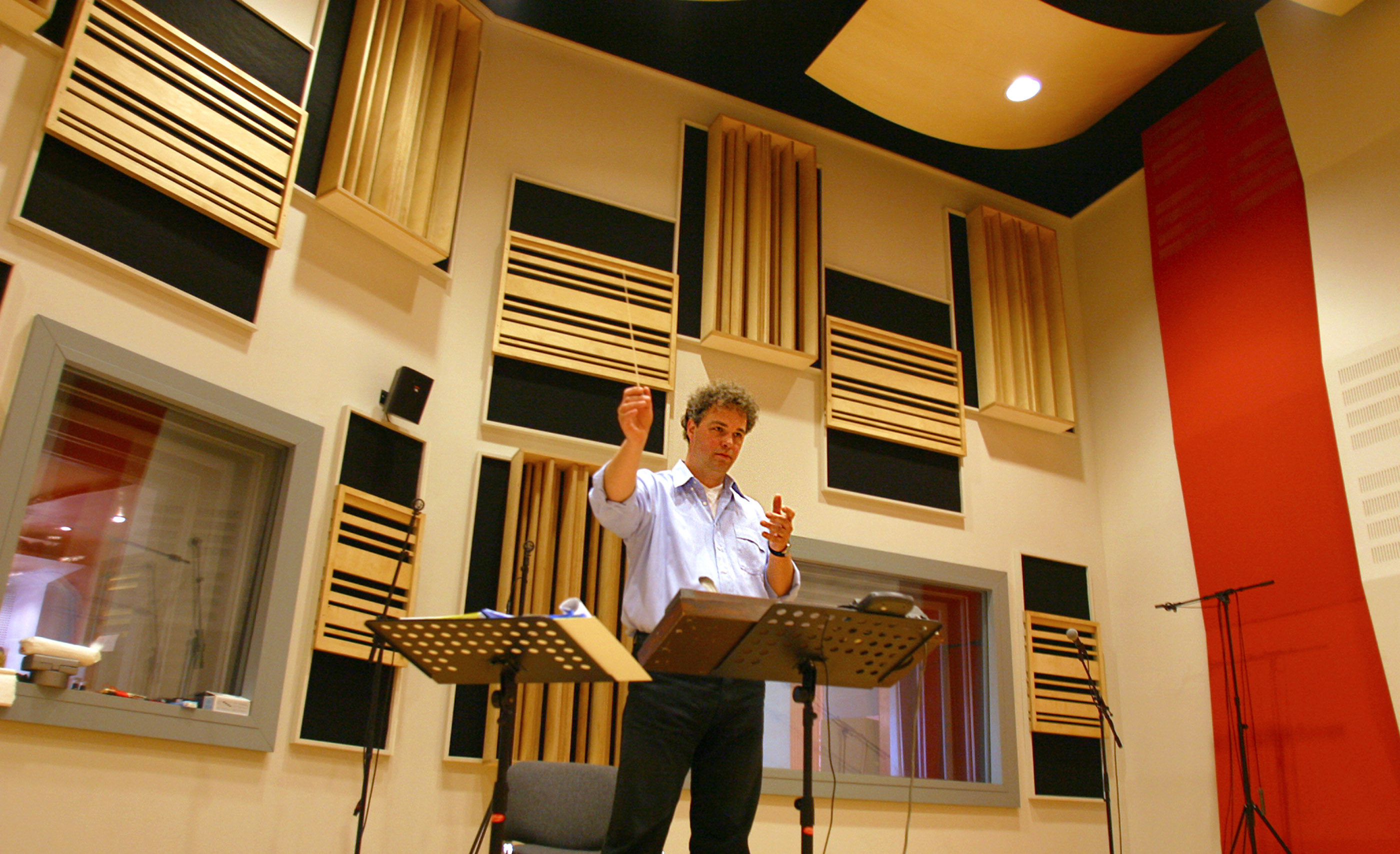 Man conducting orchestra in a professional recording studio with acoustic panels and soundproofing