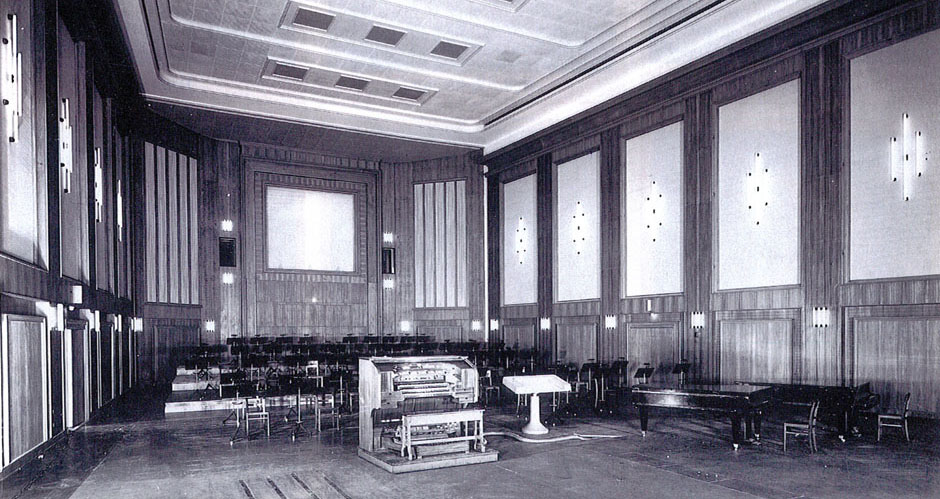 Vintage black and white photograph of an empty concert hall or scoring stage with rows of chairs, an organ, and a grand piano, showcasing 1990s music industry history.