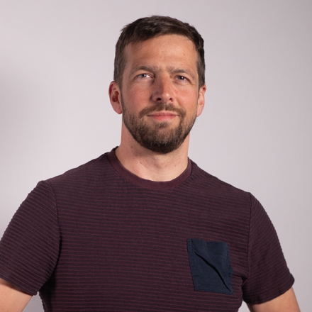 Headshot of Stefan Steinbauer, the Business Development Manager, a man with short brown hair and a beard, wearing a ribbed maroon shirt with a dark blue chest pocket, looking directly at the viewer.