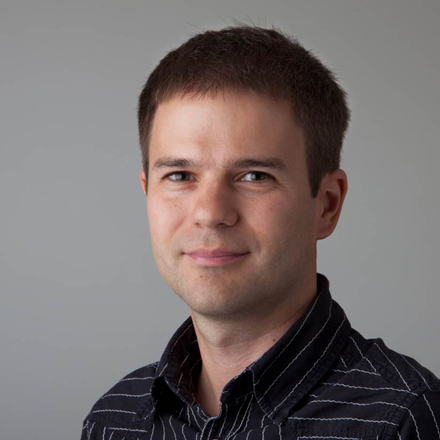 Portrait of Andreas Olszewski, responsible for percussion and preset development, wearing a striped shirt and smiling