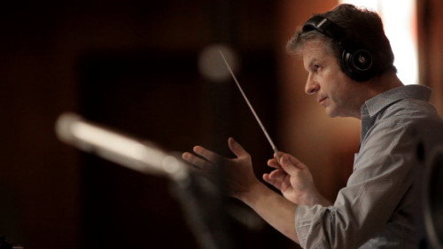 Orchestra conductor wearing headphones, holding a baton, directing the Big Bang Orchestra for Vienna Symphonic Library Synchron Instruments.