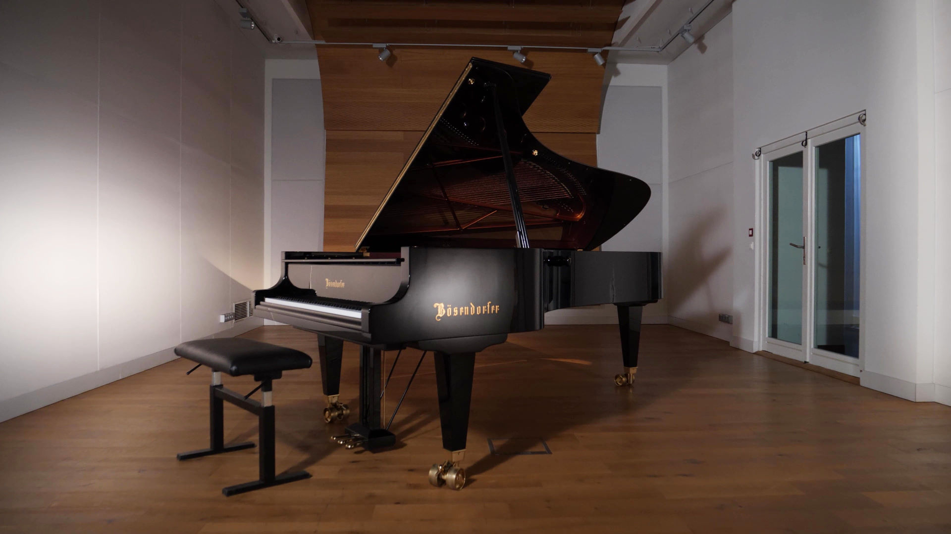 Black Bösendorfer 280VC Vienna Concert grand piano with a black piano bench on a wooden floor in a concert venue