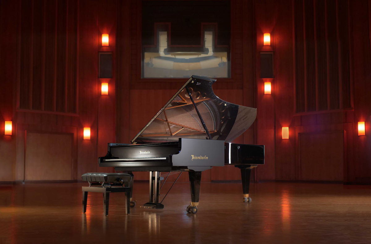Bösendorfer 290 Imperial grand piano centered in a concert hall with its lid open, showcasing its internal strings and a black leather piano bench.
