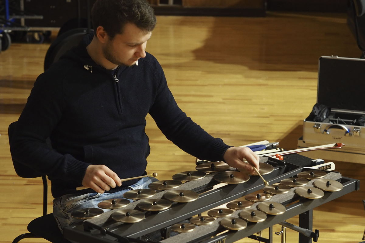 A musician in a casual blue sweater playing Synchron Percussion II tuned cymbals with mallets.