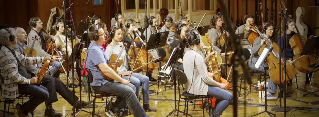 Orchestra musicians with headphones playing string instruments in a recording studio.
