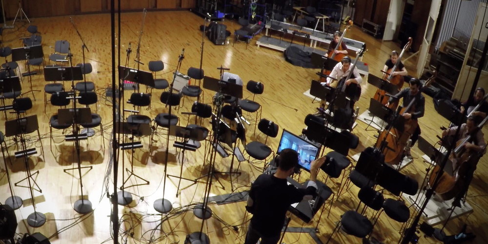 Orchestra recording session at Vienna Symphonic Library Stage A for Synchron Strings, featuring musicians playing string instruments and an audio engineer monitoring.