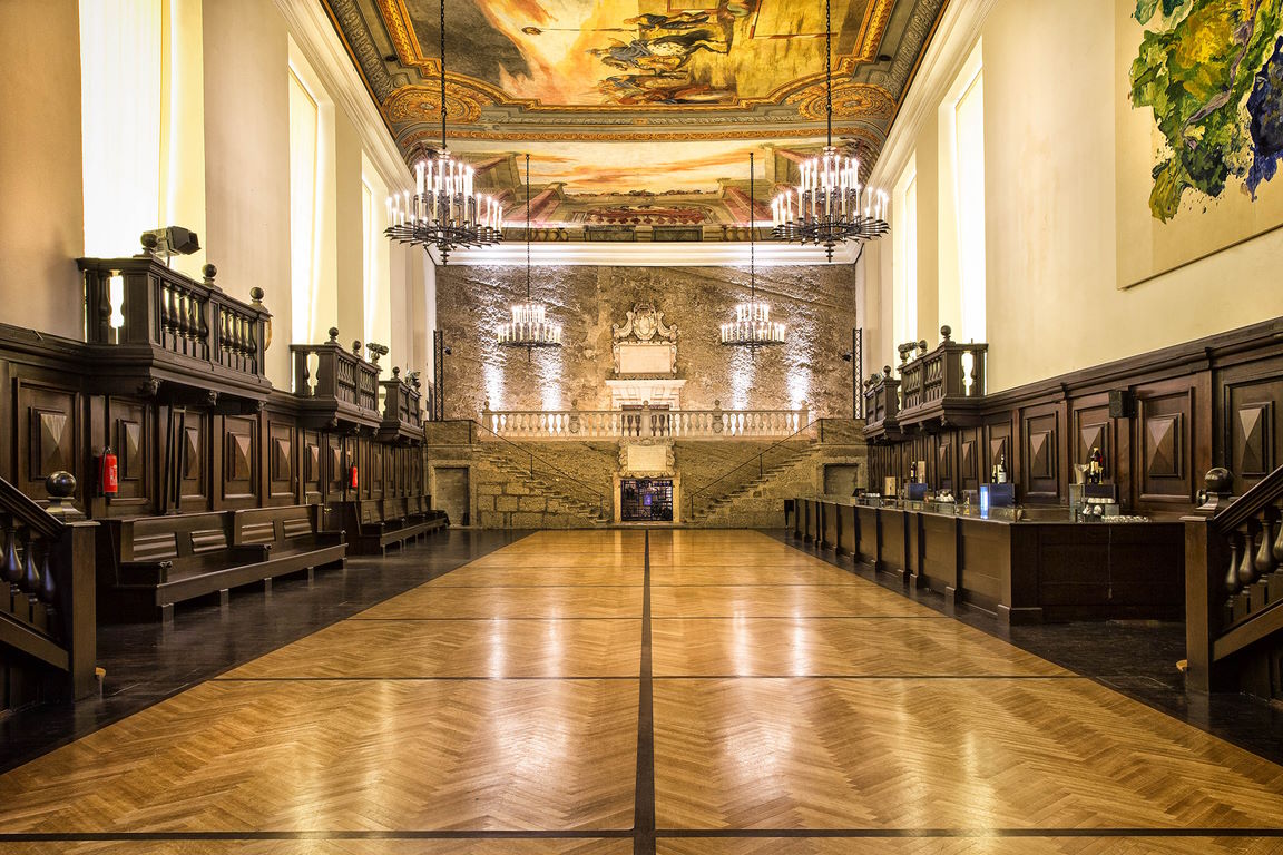 Grand interior of Grosses Festspielhaus Salzburg foyer featuring an ornate painted ceiling, large chandeliers, dark wood paneling, and a stone staircase.