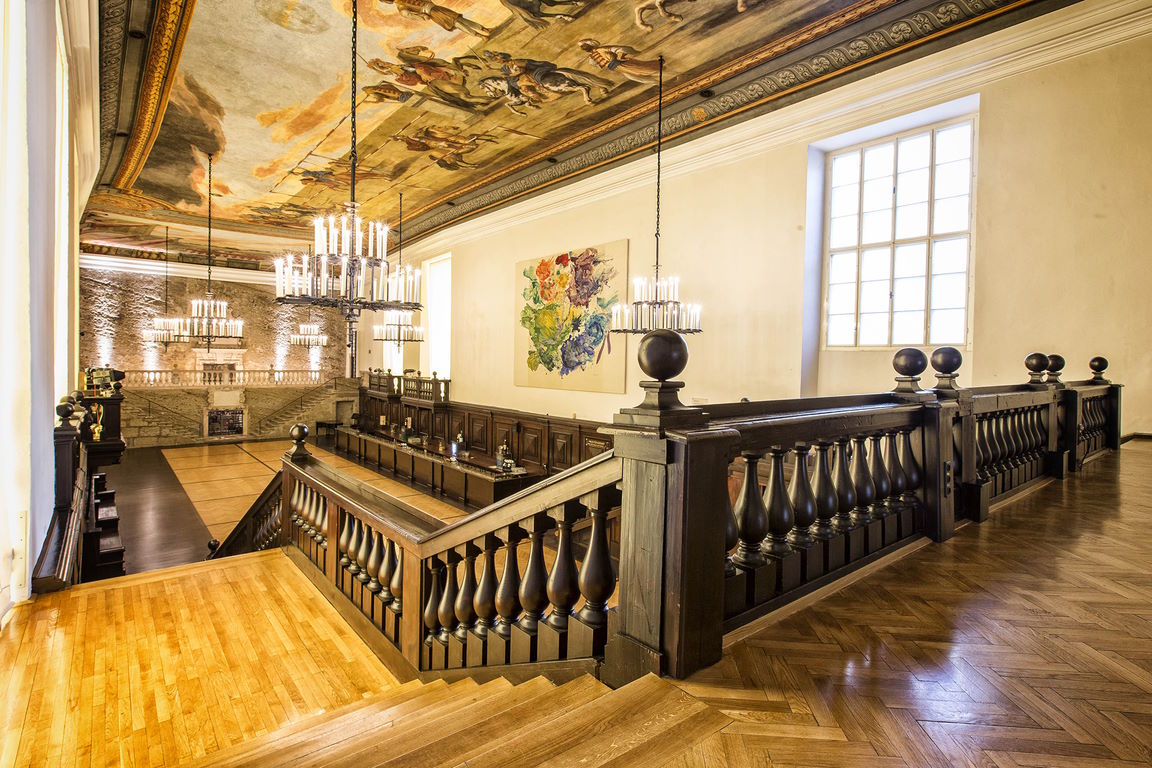 Grand interior of Grosses Festspielhaus Salzburg foyer showcasing a frescoed ceiling, massive chandeliers, wide wooden staircases, and historic architectural details.