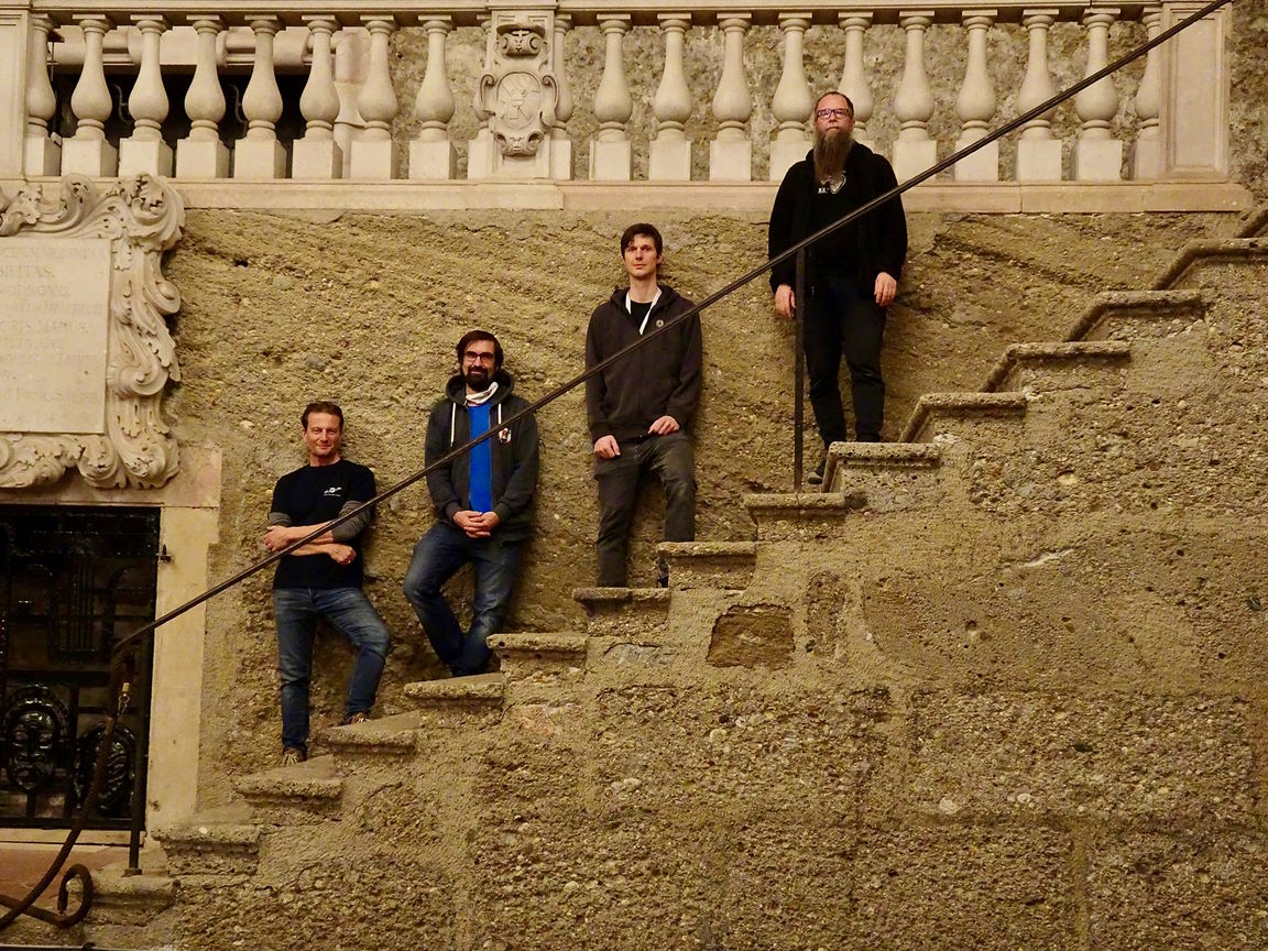 Four men, part of the Vienna MIR RoomPack 7 team, stand on the textured concrete staircase of Grosses Festspielhaus Salzburg.