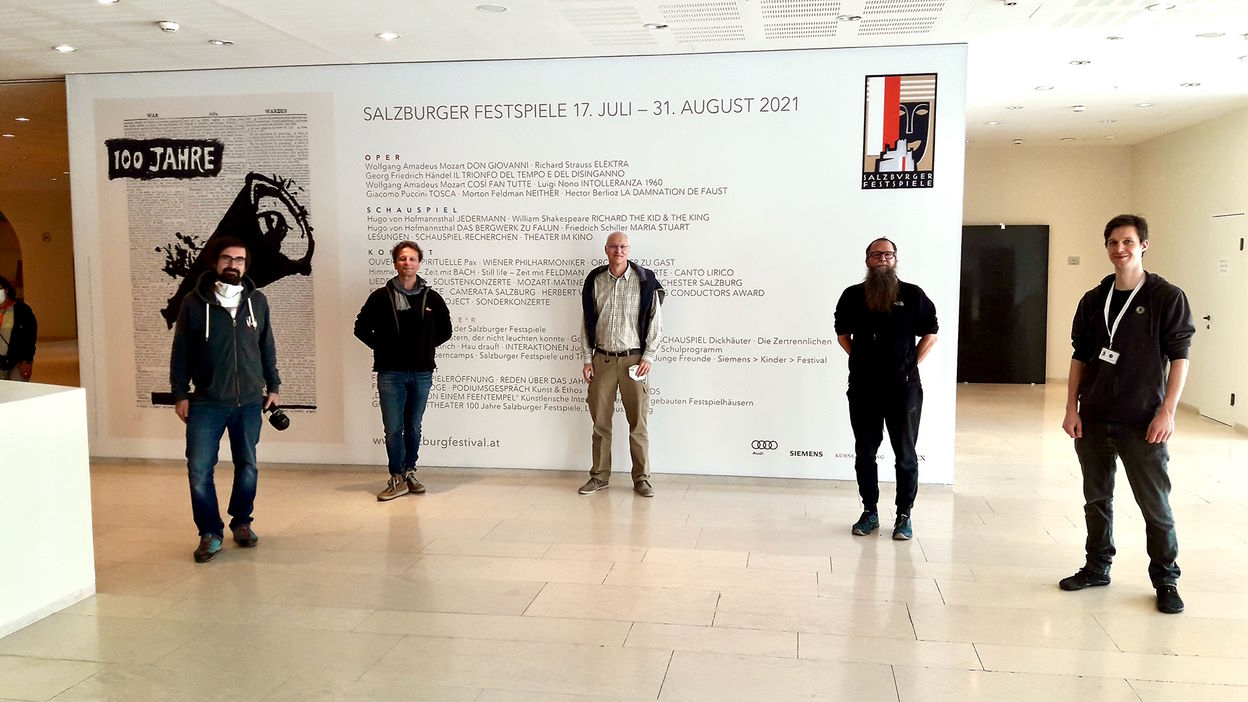 Five men standing in front of a white wall with the Salzburg Festival program for July-August 2021