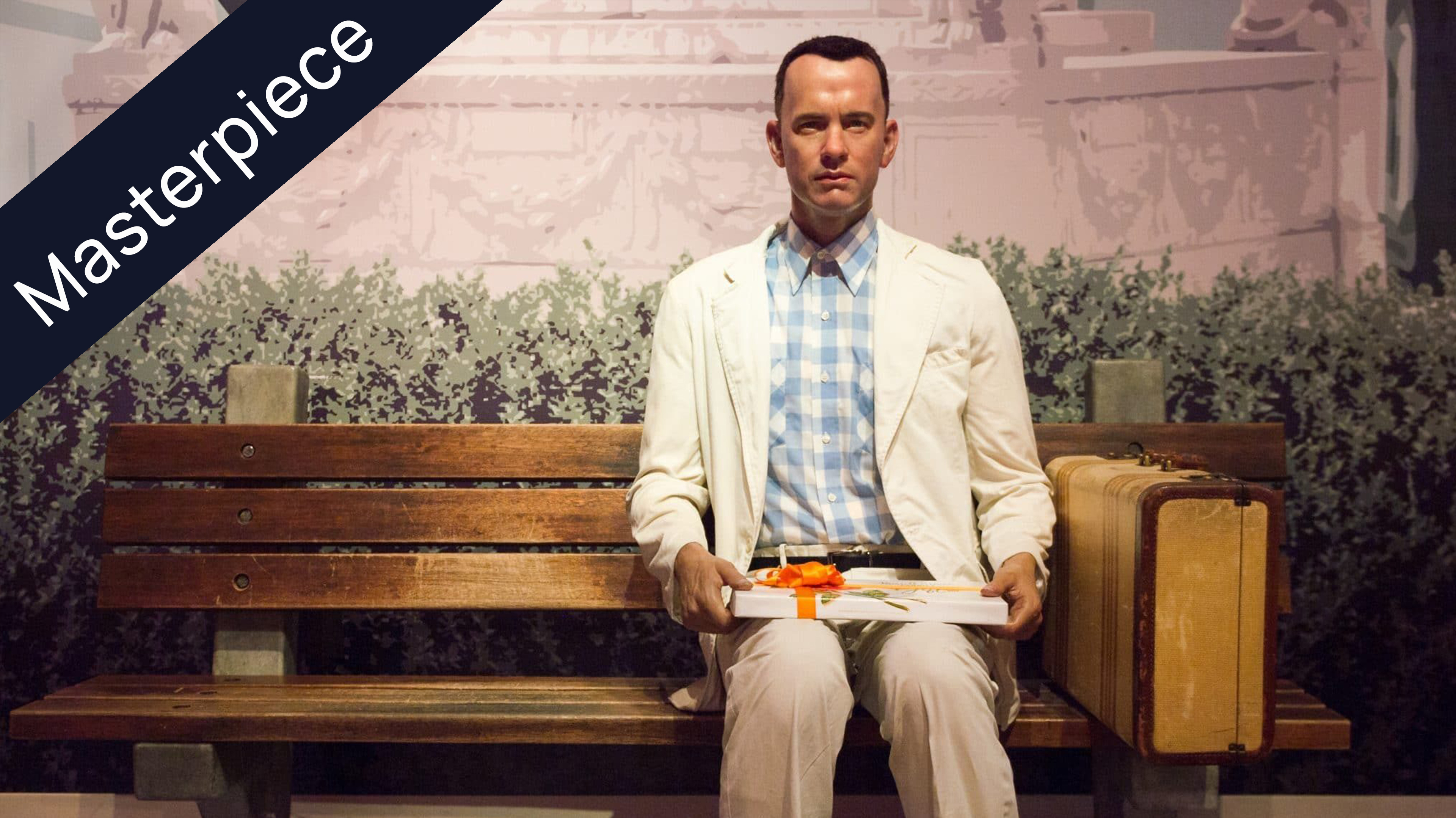 Tom Hanks as Forrest Gump sitting on a park bench, holding a box of chocolates, with a suitcase beside him.