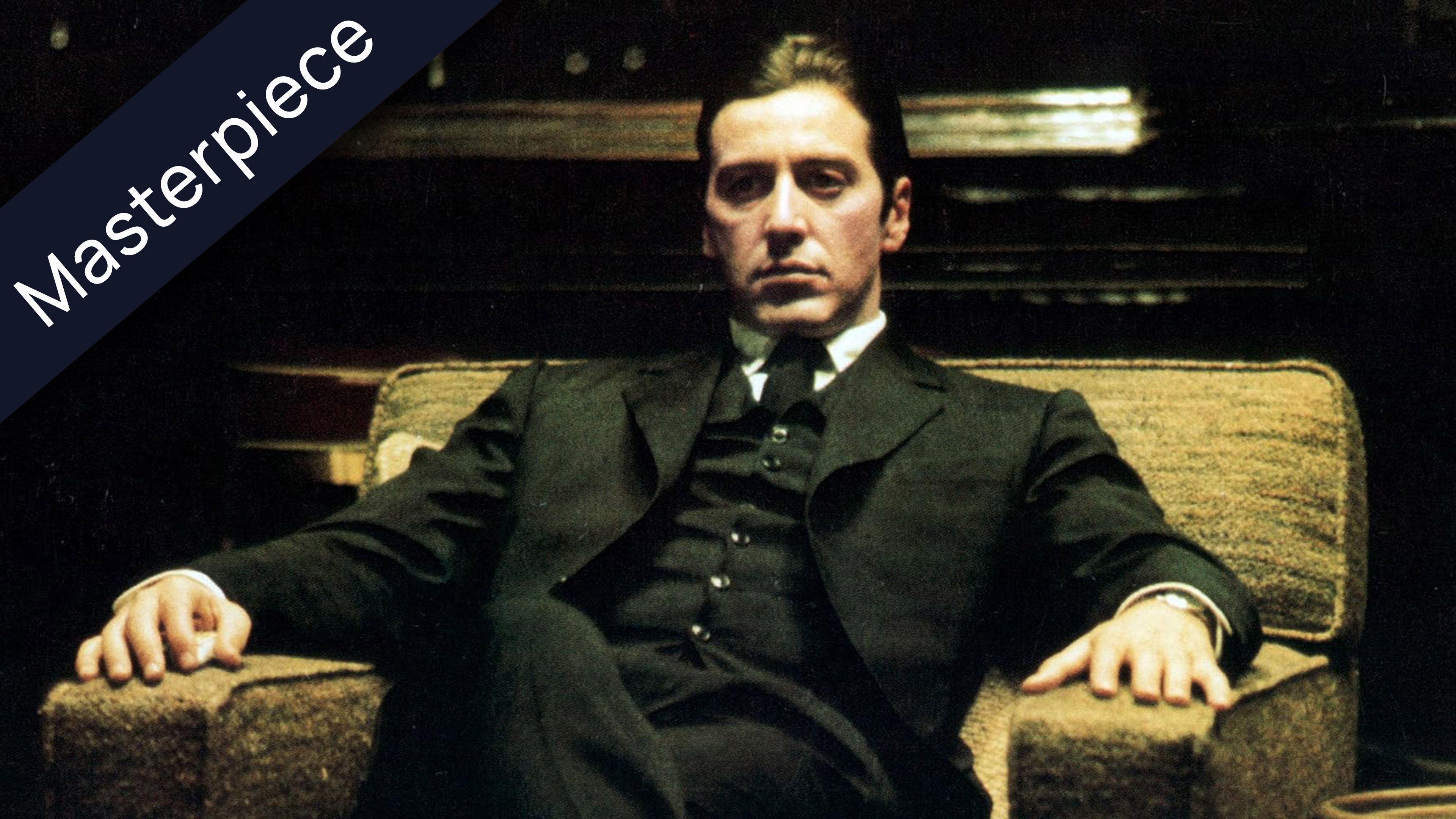 Al Pacino as Michael Corleone in The Godfather, seated in a chair, wearing a dark suit and tie, with a Masterpiece banner in the upper left corner.