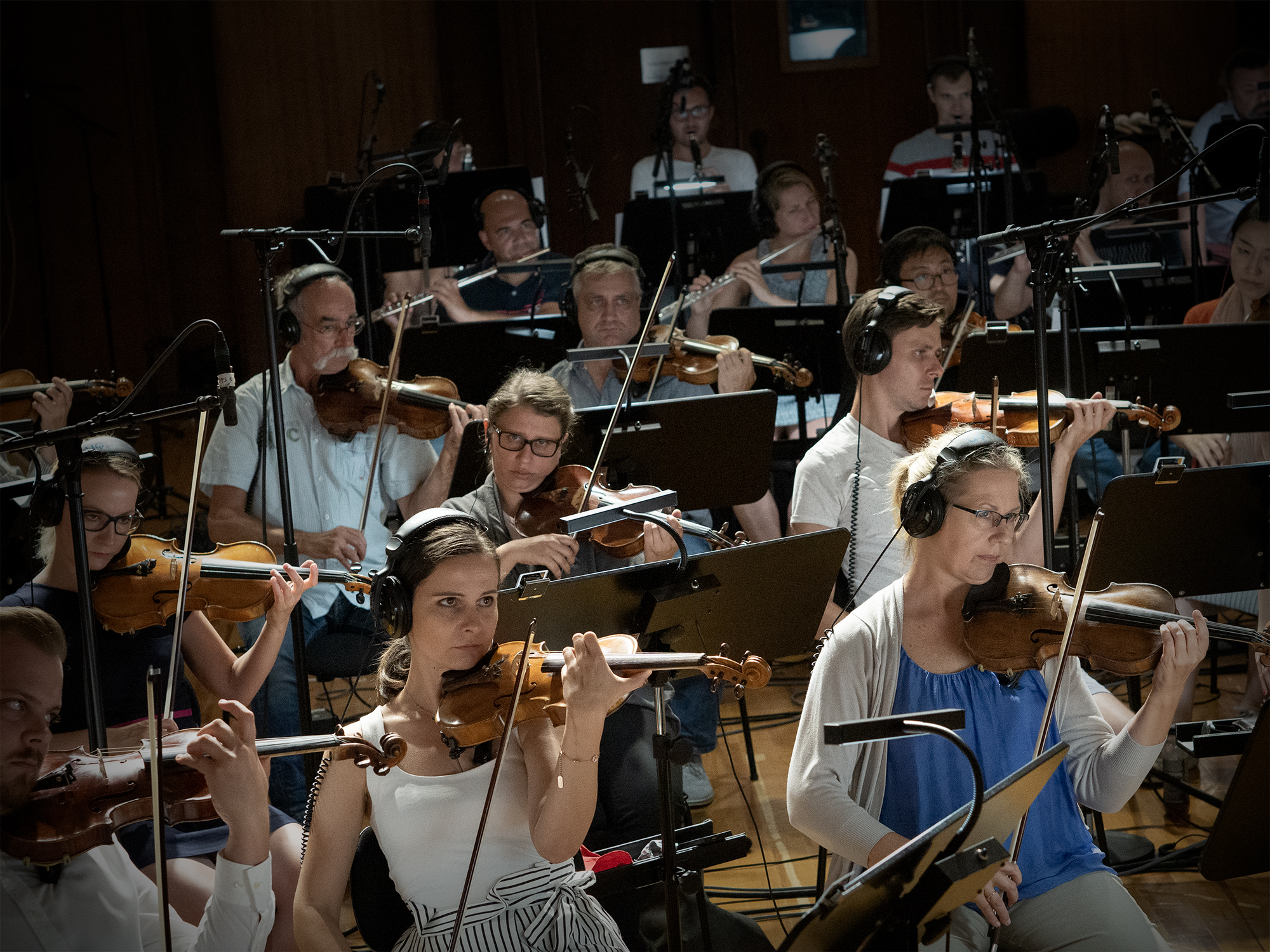 Orchestra musicians performing with violins and flutes in a recording studio.