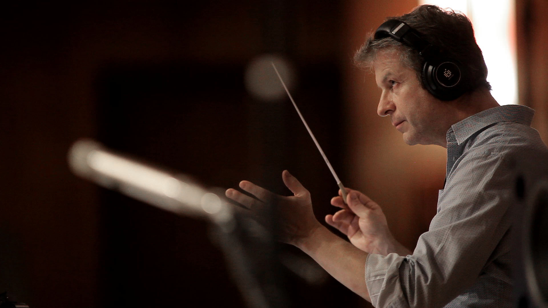 Man in headphones conducting with a baton in a recording studio.