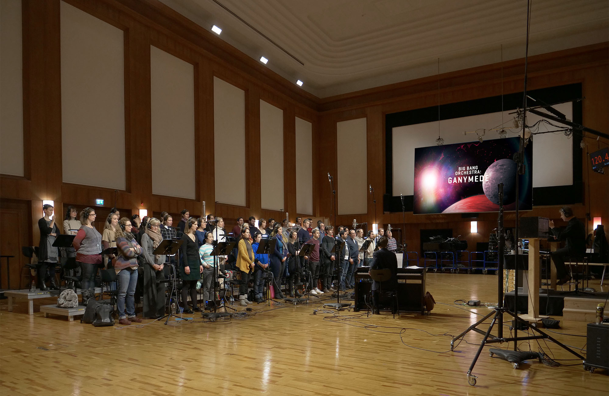 Choir and orchestra recording Big Bang Orchestra Ganymede in a large studio with wooden walls and flooring.