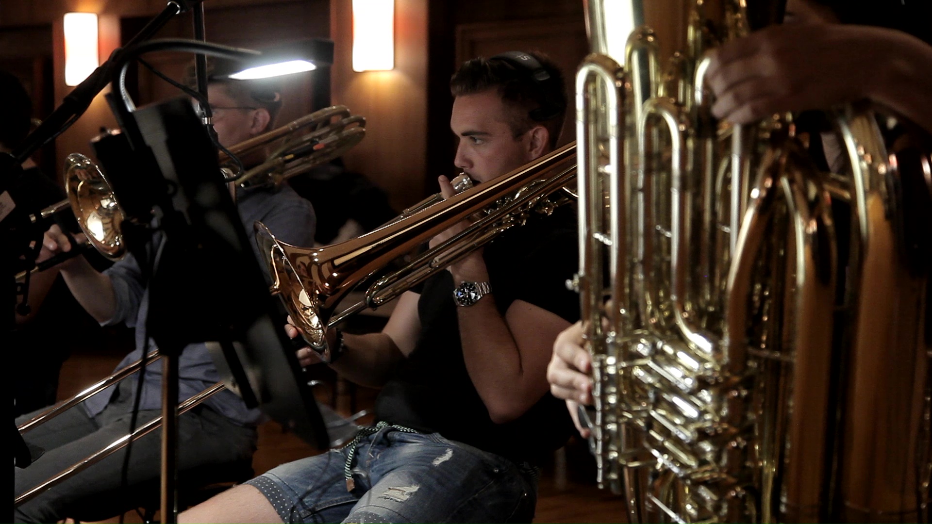 Brass musicians playing instruments in an orchestra or band, with a focus on a trombone player and visible tuba parts.