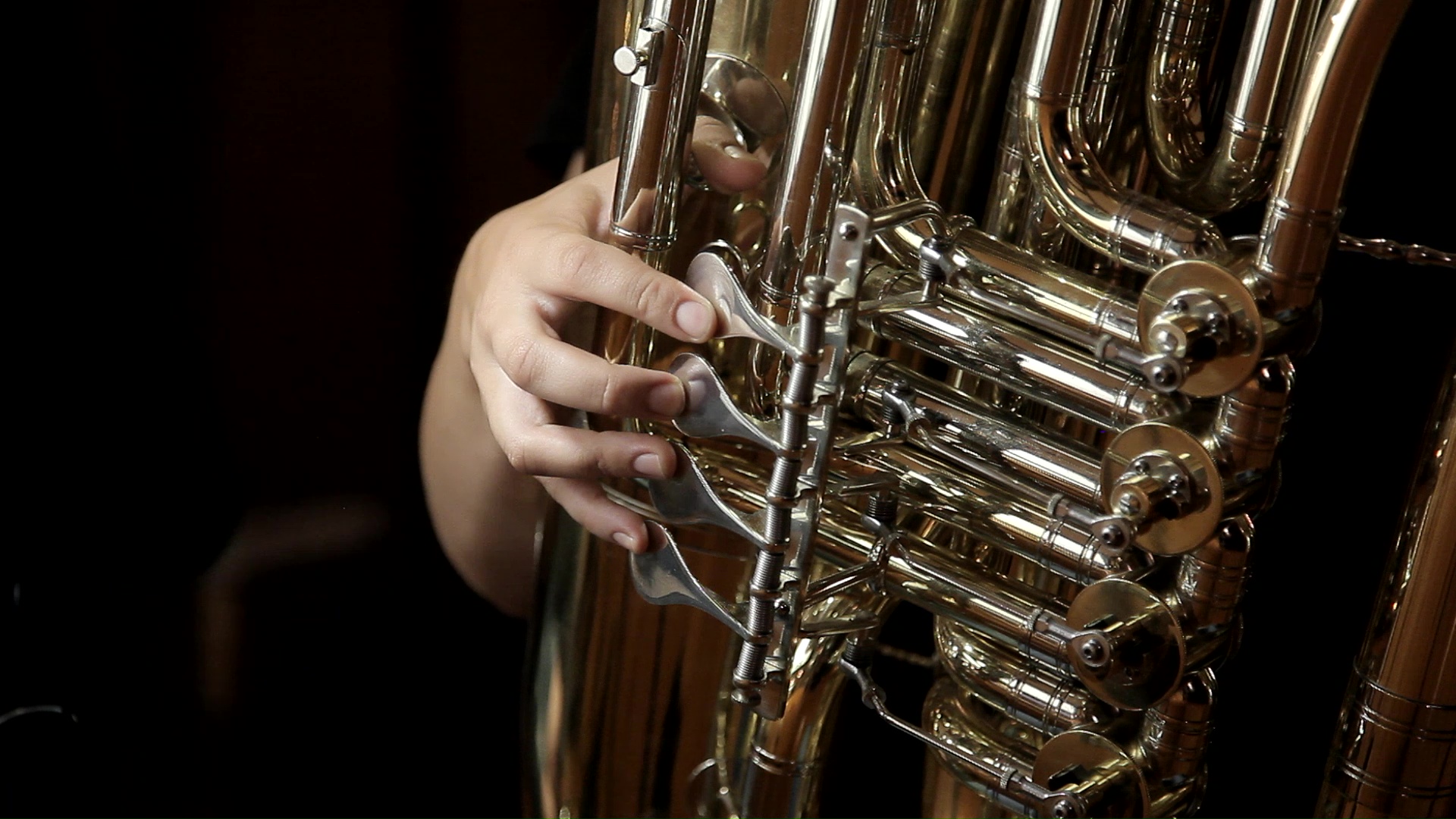 Musician's hands expertly pressing the valves of a brass tuba, showcasing the shiny keys, tubing, and intricate details of the musical instrument.