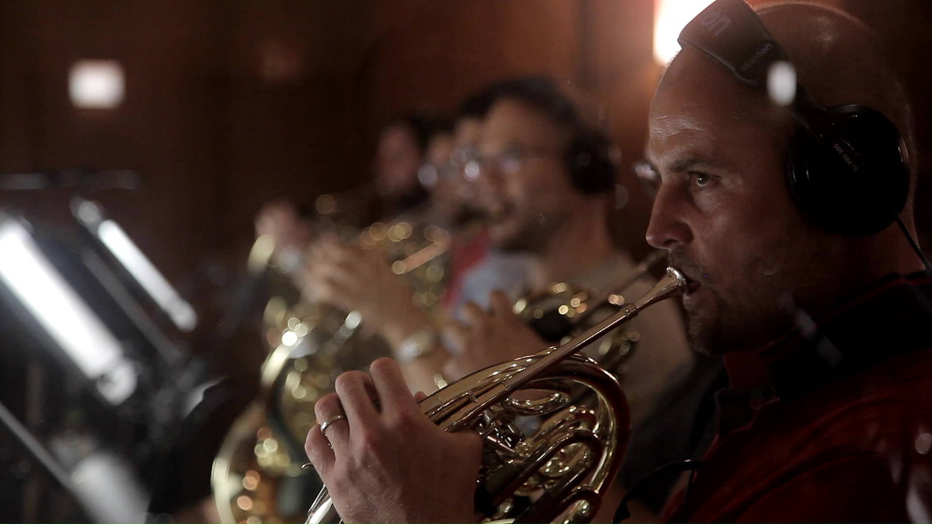 Musician wearing headphones playing a brass instrument like a French horn in an orchestra or recording studio.
