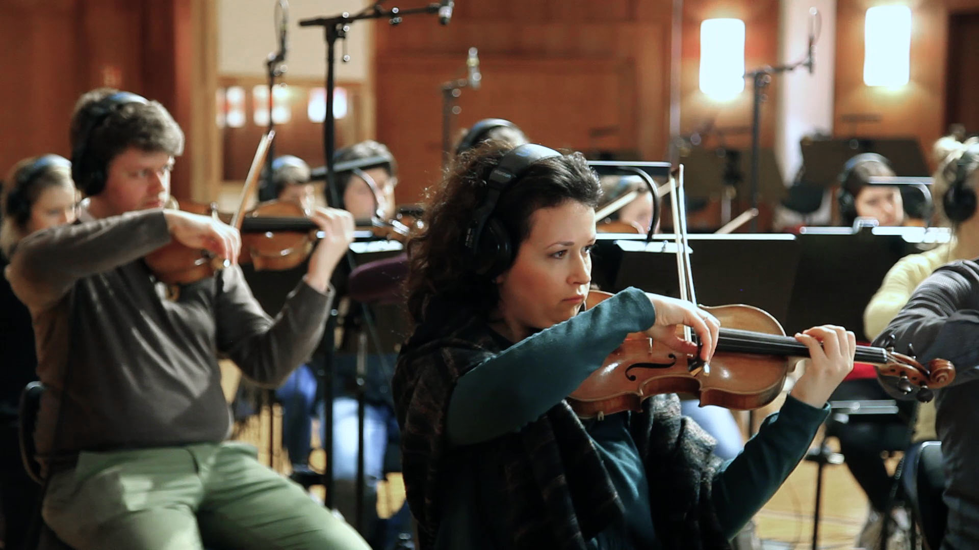 Musicians in headphones playing violins and other string instruments during an orchestra recording session in a studio.