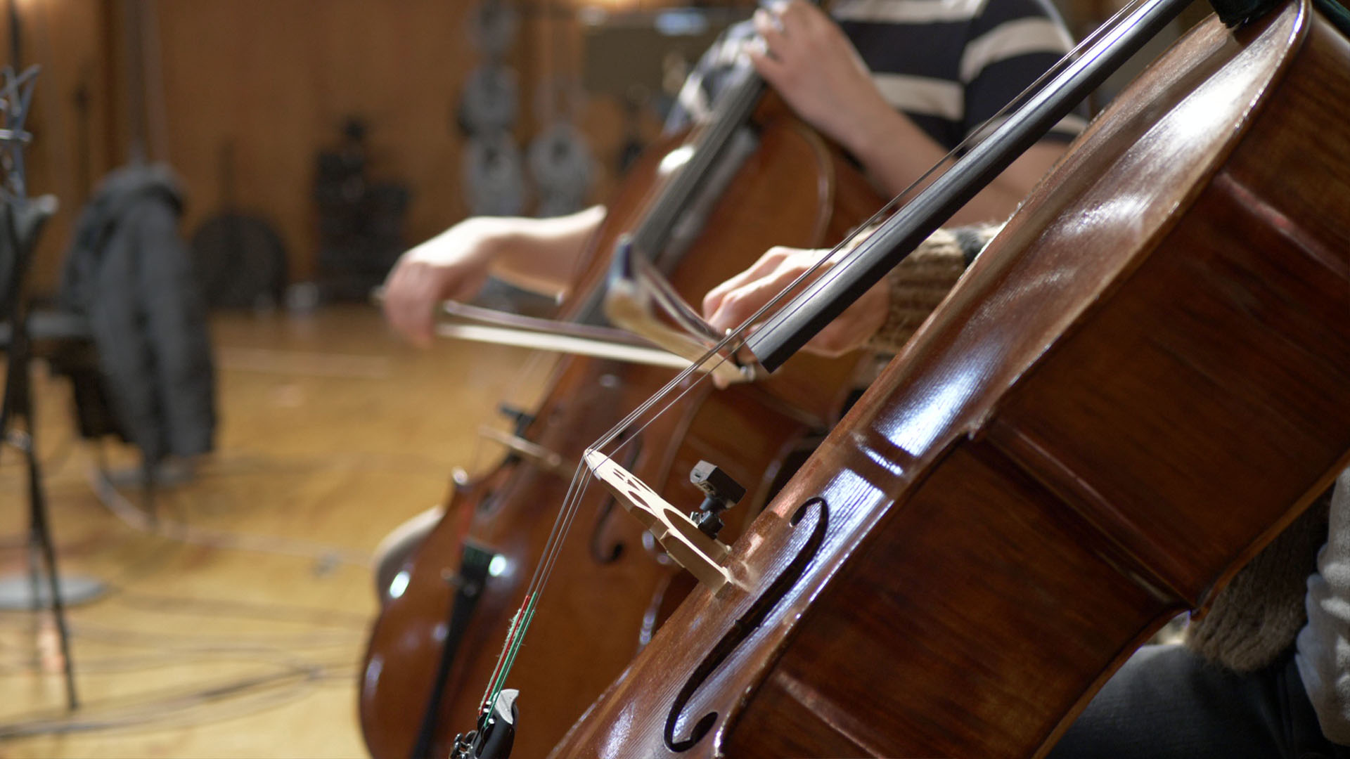 Close-up of three cellos being played by musicians in an orchestra during a musical performance or practice session.
