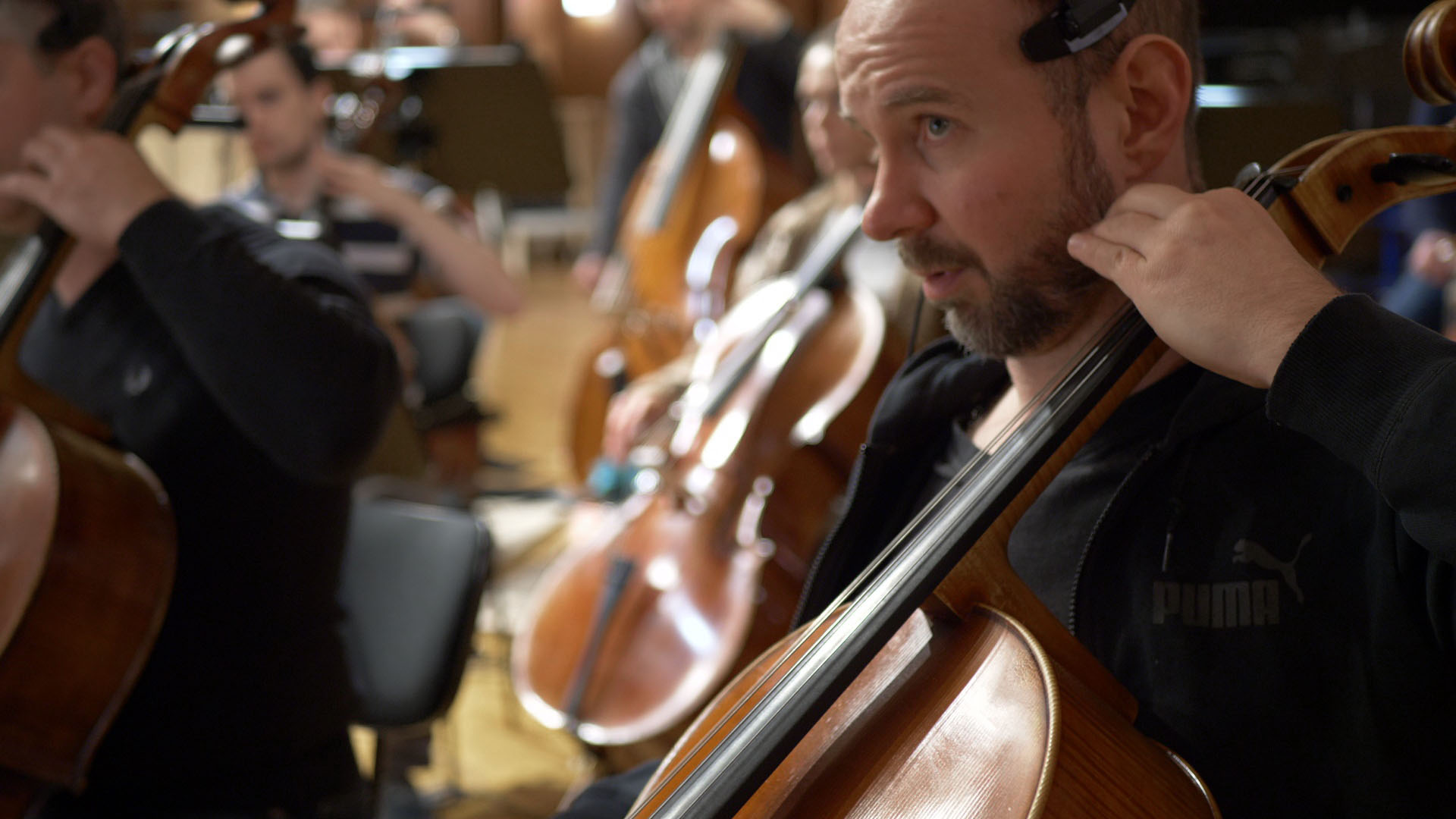 Orchestra cellist in black Puma hoodie playing string instrument during performance