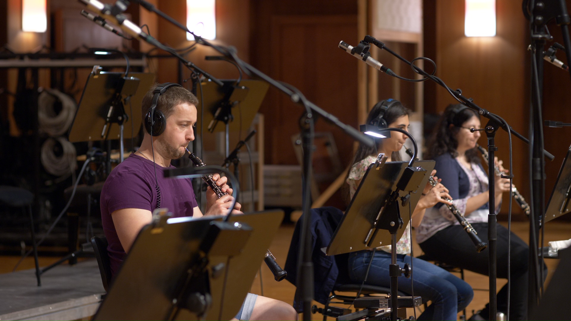 Musicians playing oboes in a recording studio, with microphones and music stands.