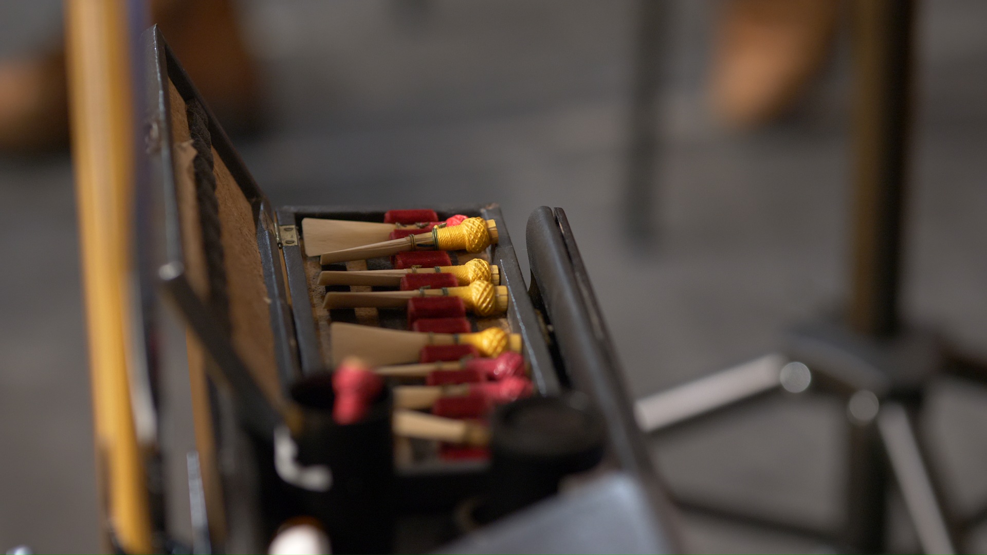 Close-up of a wooden oboe reed case containing several light brown oboe reeds with red and yellow thread bindings.