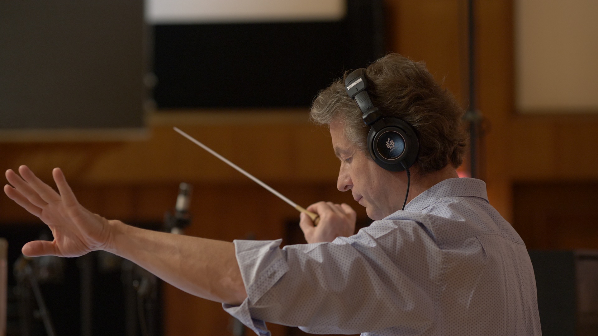 A male conductor with headphones and a batoning hand in the middle of conducting an orchestra