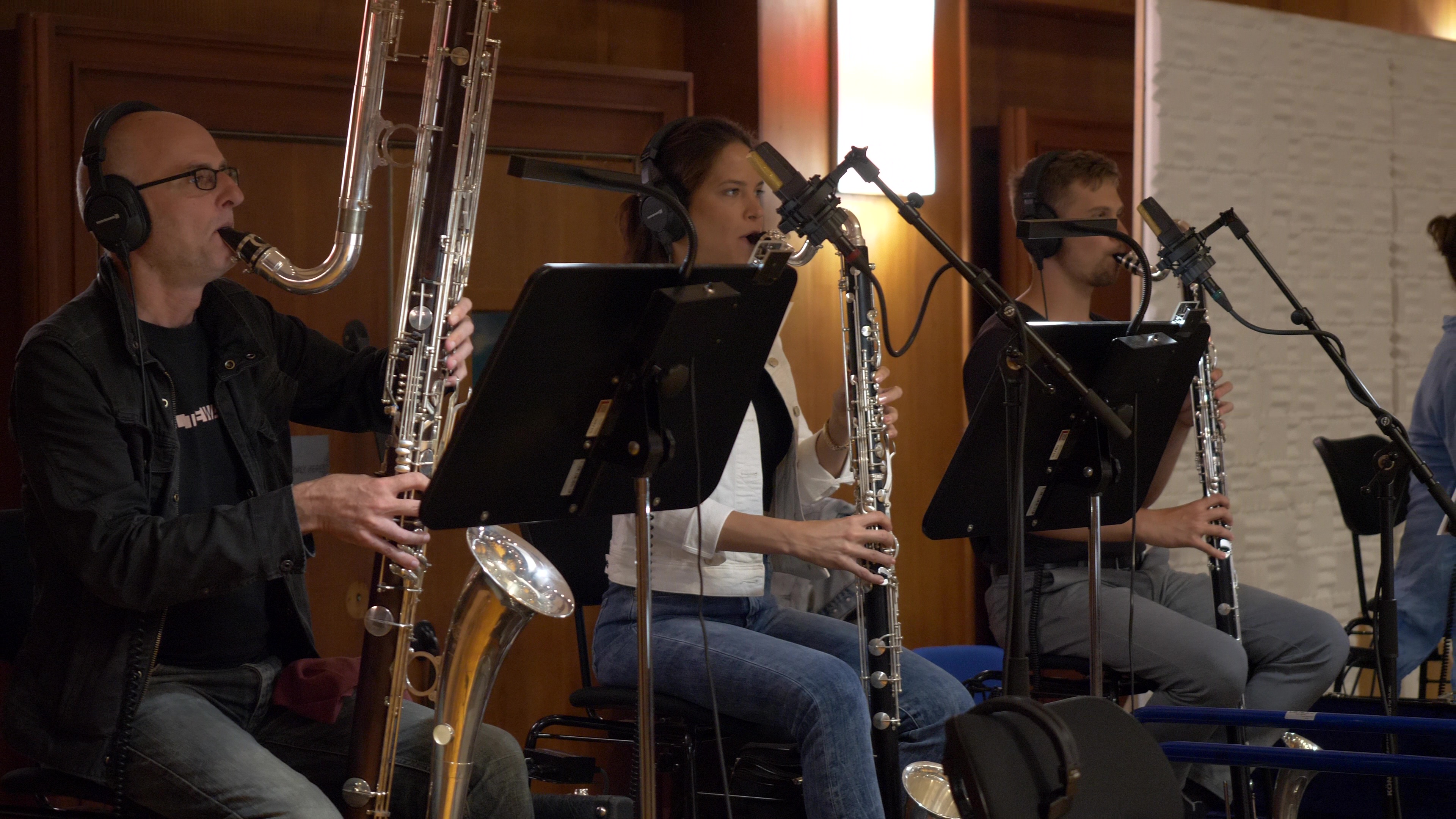 Musicians recording woodwind instruments in a studio, including a bass clarinet, contrabass clarinet, and possibly an oboe.