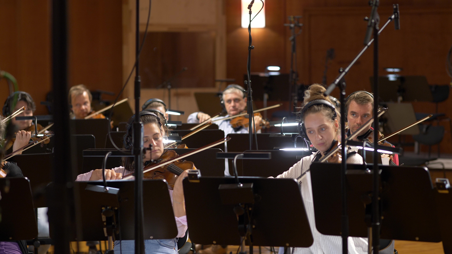 Musicians with headphones playing violins in a recording studio, highlighting the live orchestra session.