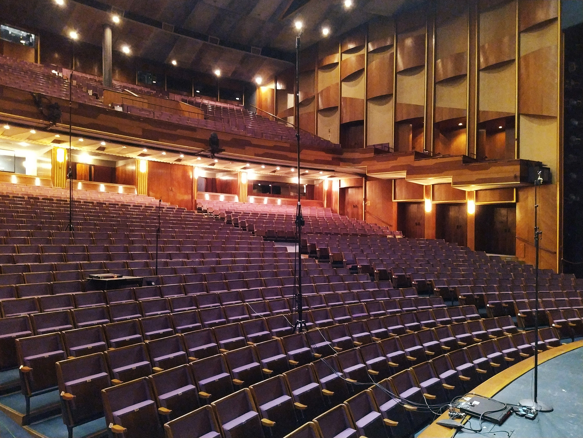 Empty theater with rows of purple seats and wood paneling, lit by warm lights.