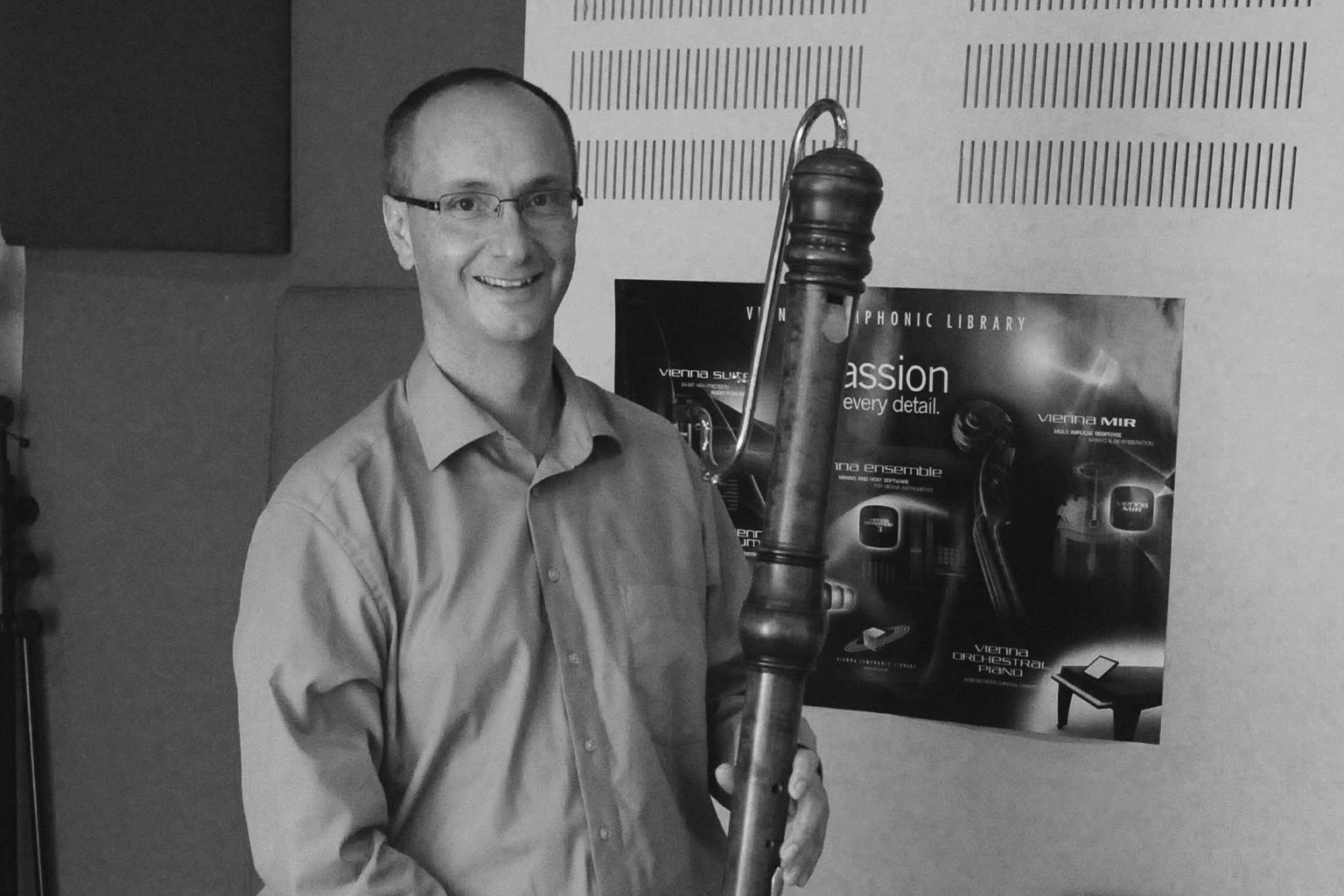 A man holding a bassoon, smiling next to a Vienna Symphonic Library poster.