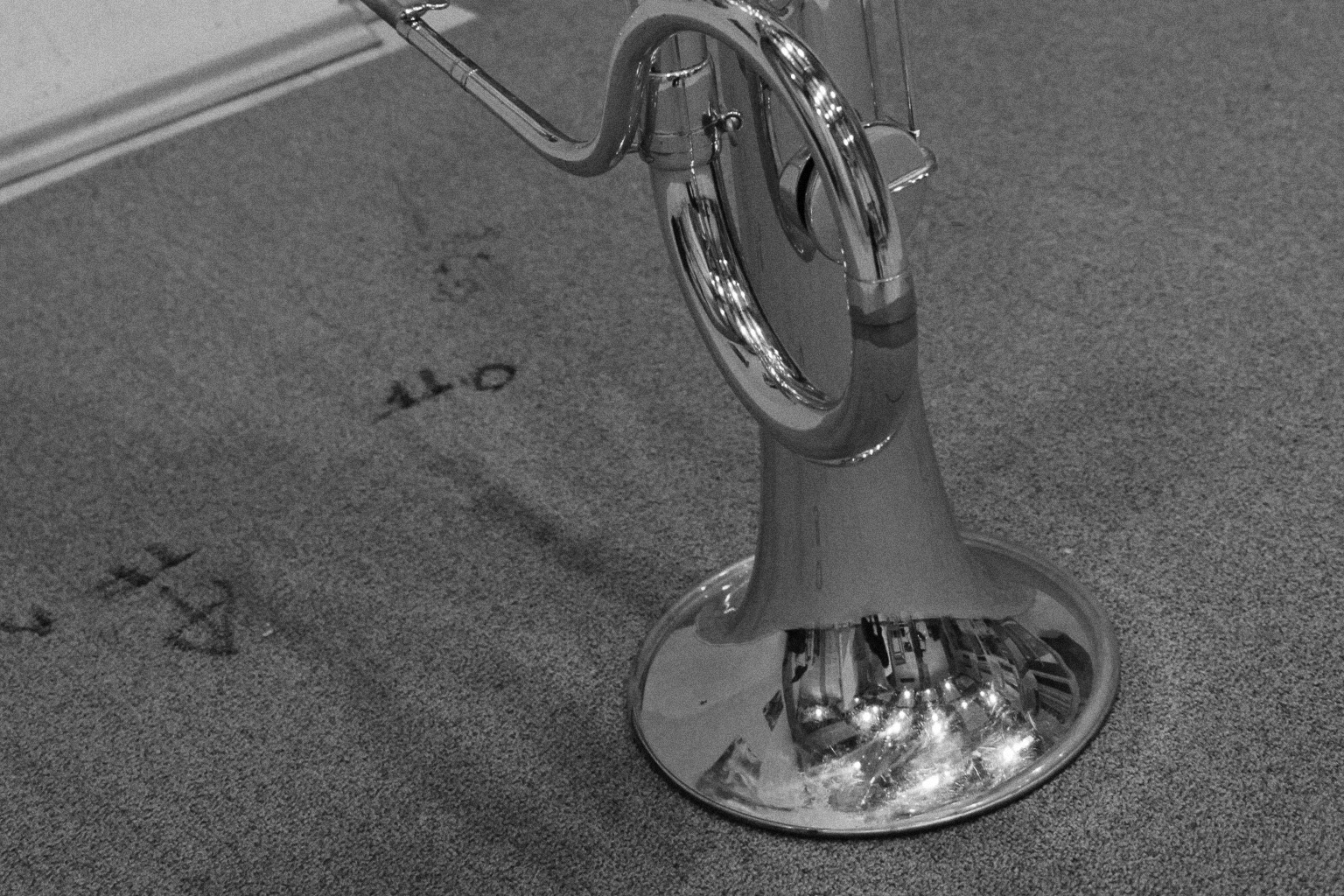 Black and white image of a shiny brass baritone instrument with a large bell reflecting lights, resting on a gray textured carpet with 440 written on it.