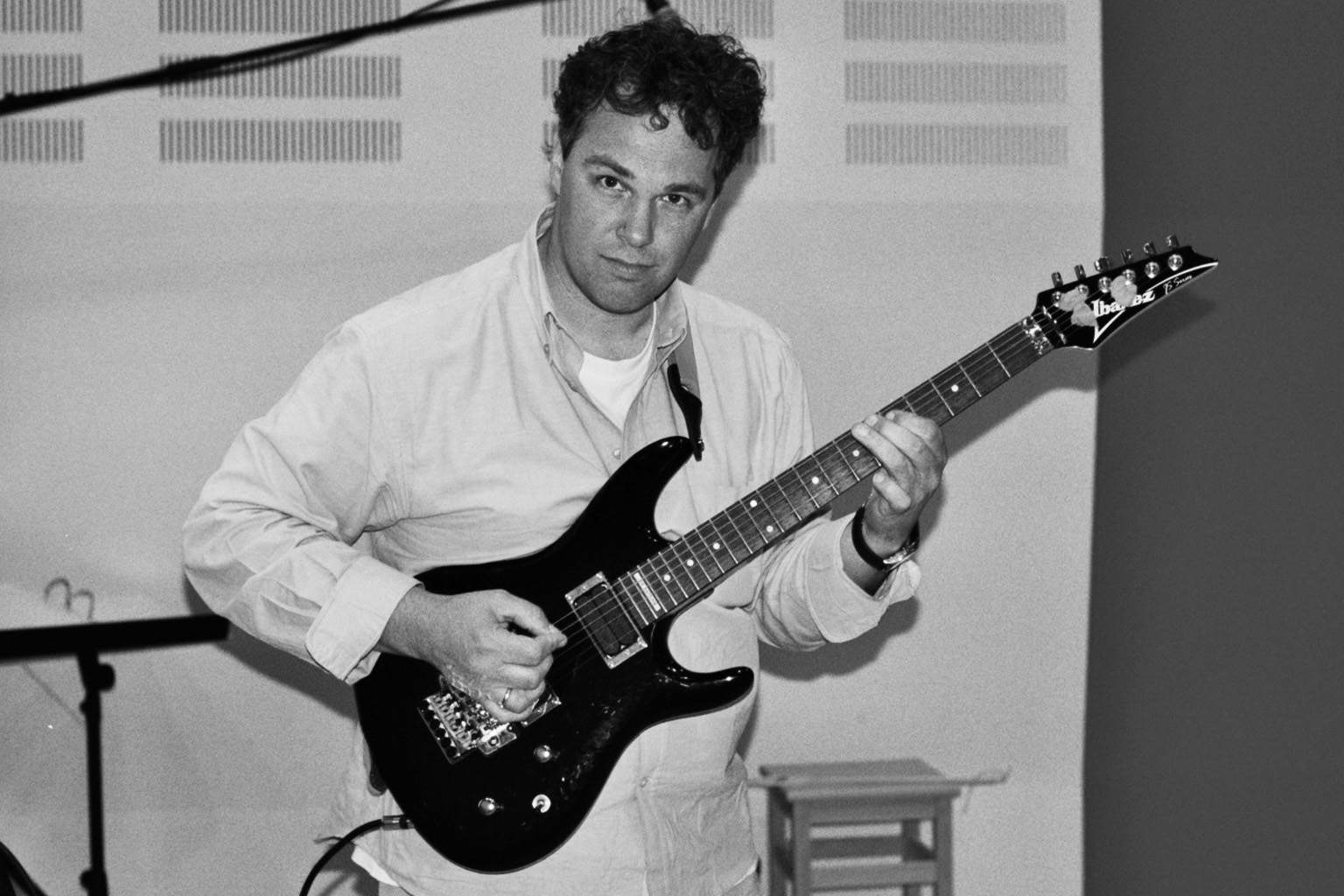 Black and white photo of a man with curly hair playing an Ibanez electric guitar.