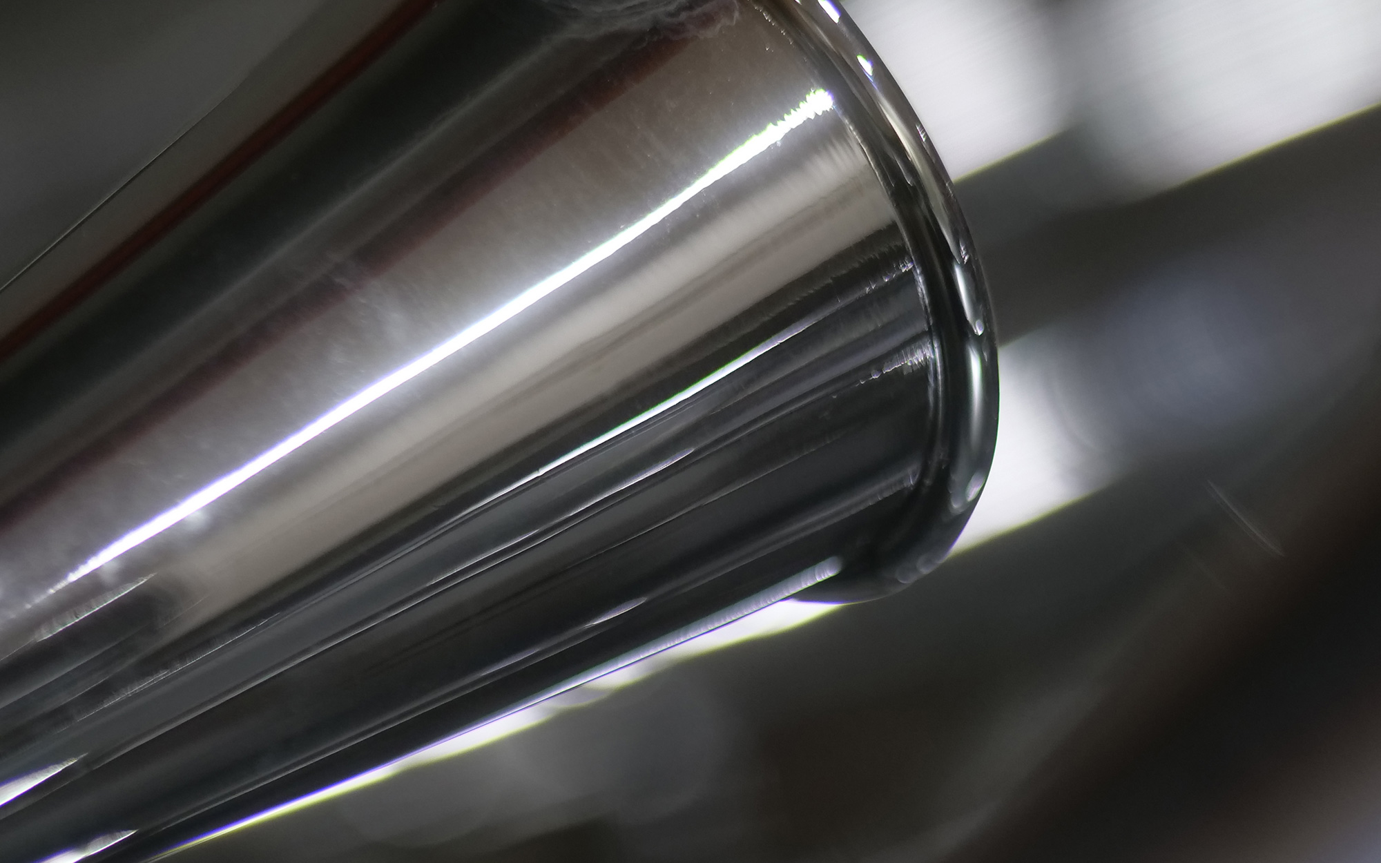 Abstract cylindrical metallic object or pipe reflecting light, showcasing shiny textures and parallel lines.