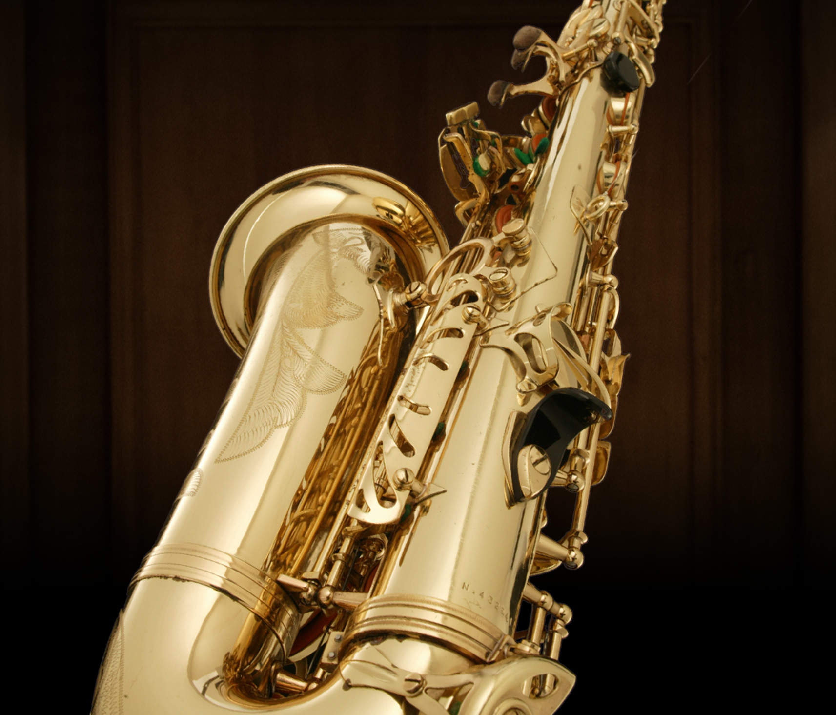 Shiny gold brass saxophone with detailed engravings on the bell, set against a dark background showcasing its intricate keys and polished finish.