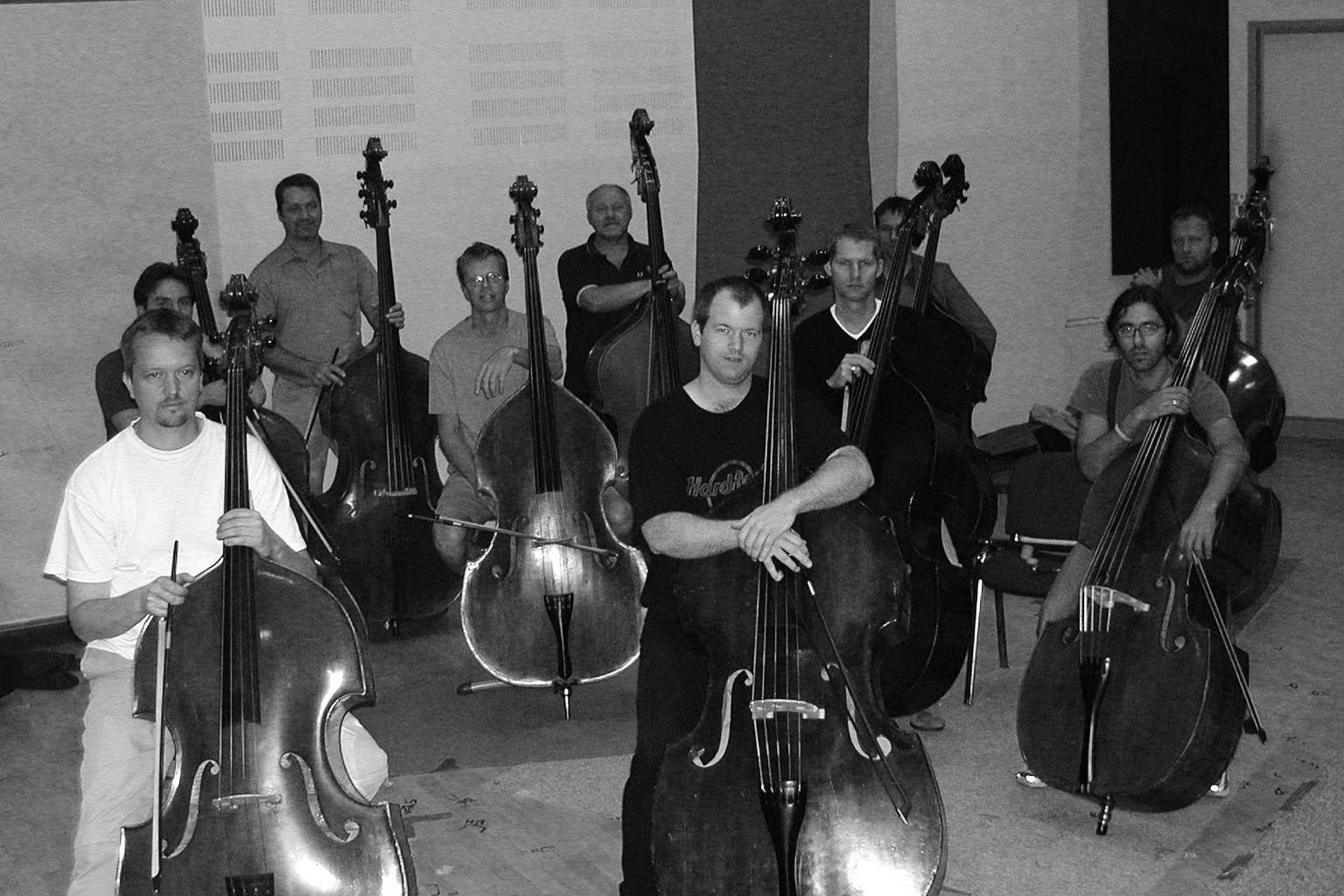 Black and white photo of a group of male musicians with several large string basses in a room.