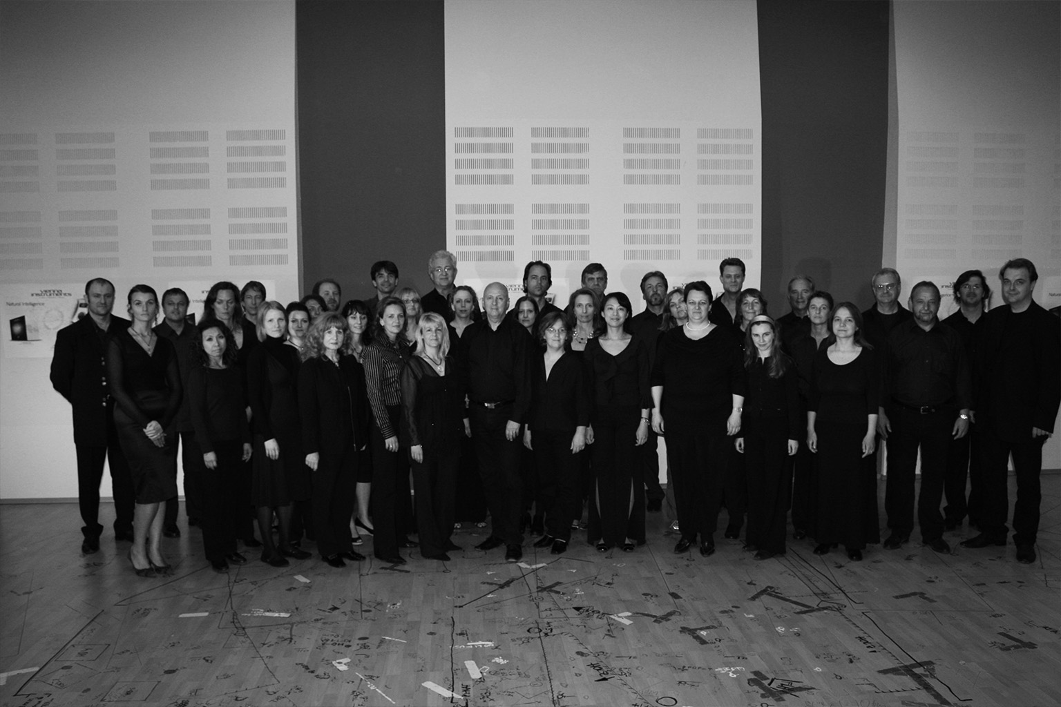 Group photo of a large choir, approximately 40 male and female singers of varying ages, all dressed in formal black attire, standing together for a portrait.