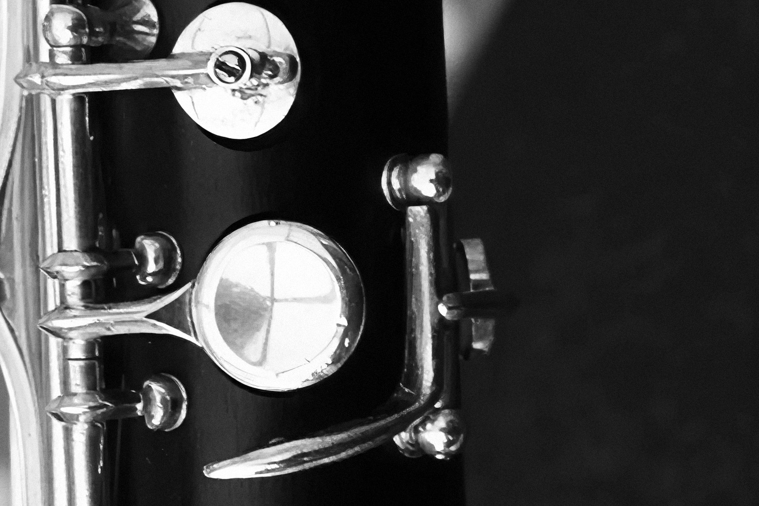 Black and white close-up of a clarinet's glossy black body with shiny metallic keys and mechanisms, showcasing its intricate musical instrument details.