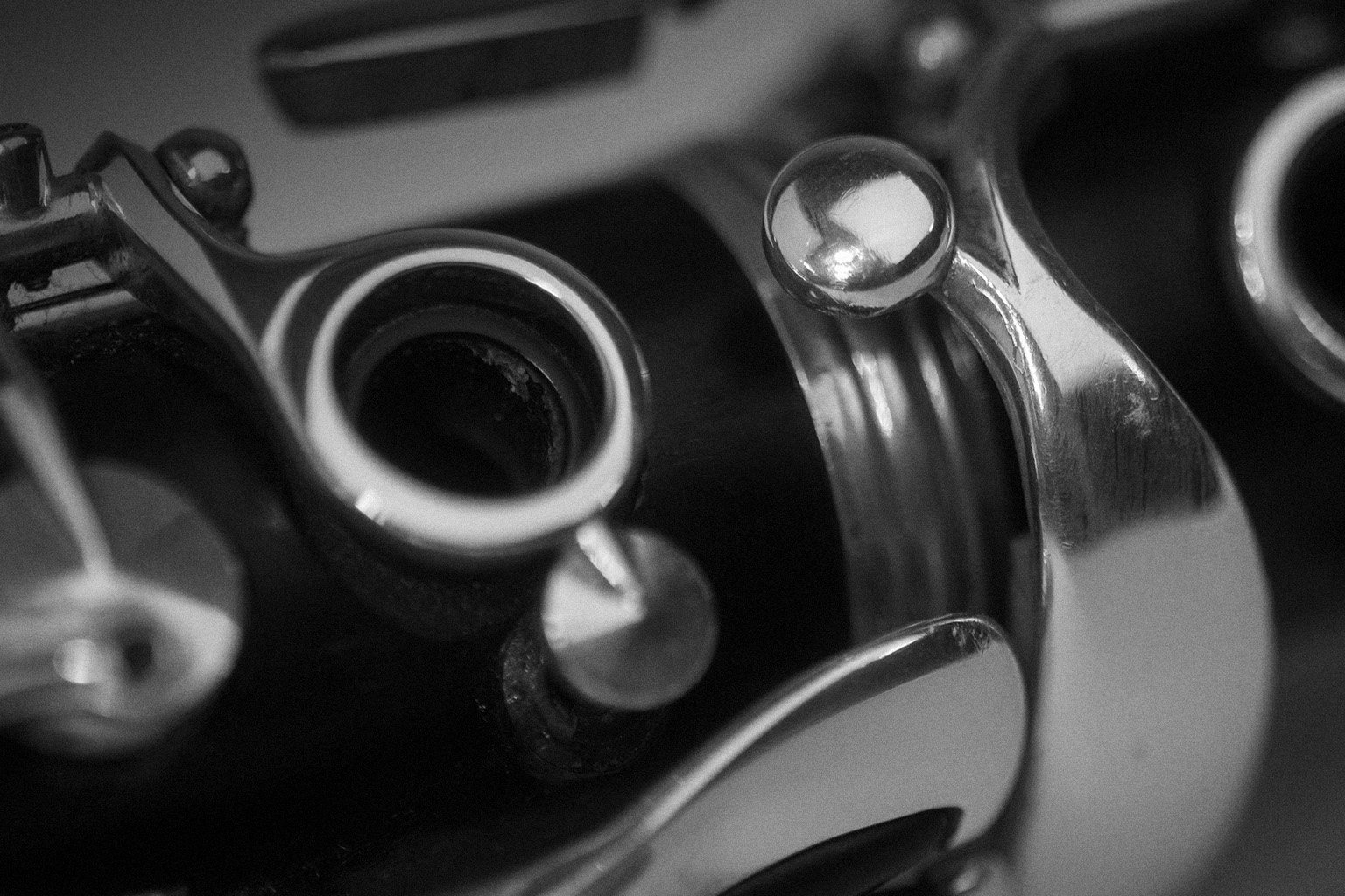 Close-up monochrome view of a clarinet, showcasing its intricate keys, metallic levers, and reflections, highlighting the design details of the woodwind instrument