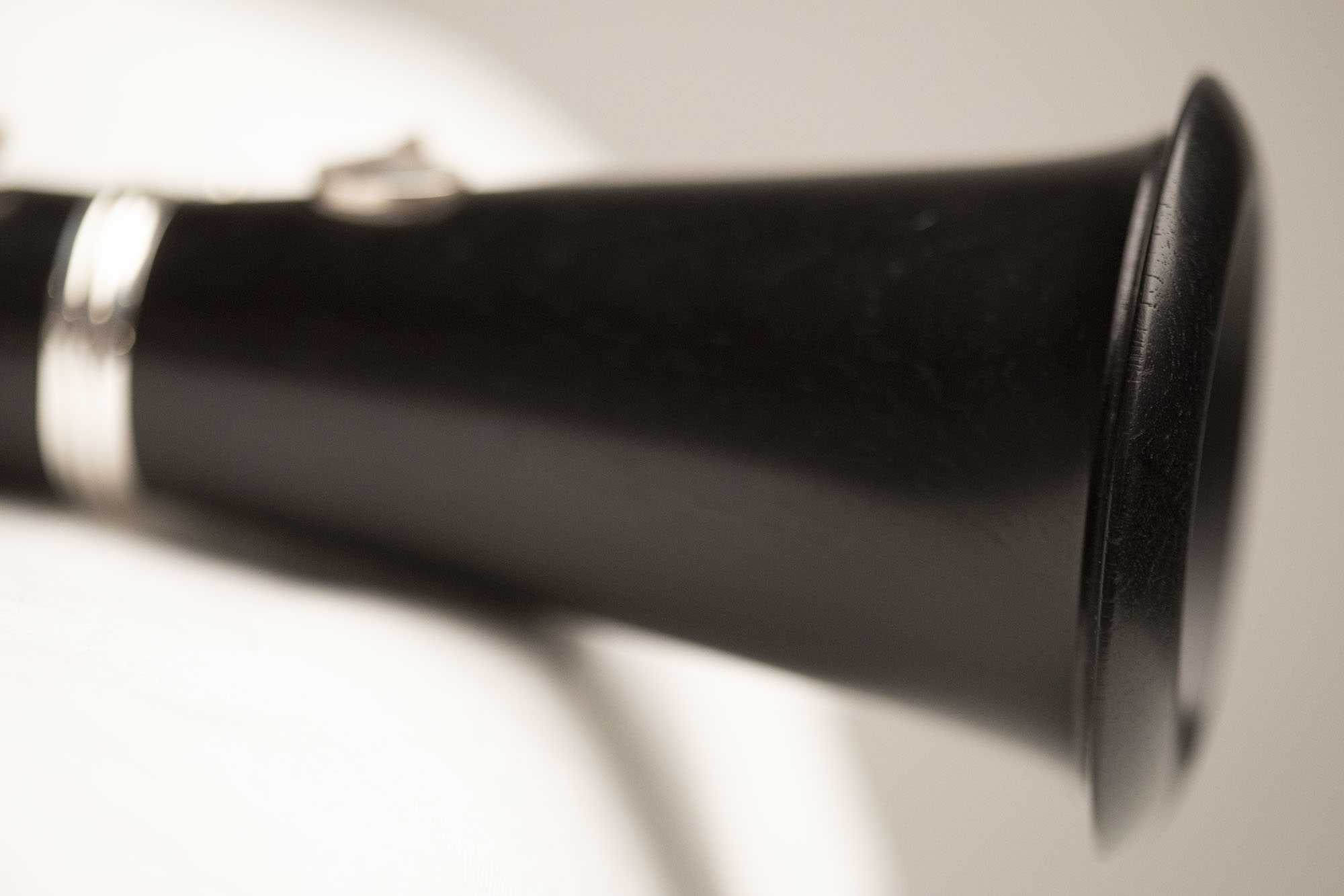 Close-up of a black clarinet, showing the bell and silver accents against a light background.