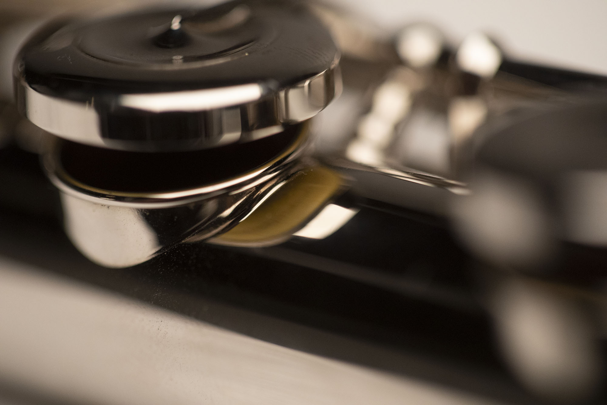 Close-up of a silver flute key mechanism with shiny metal pads and dark reflections, showcasing the instrument's intricate details.