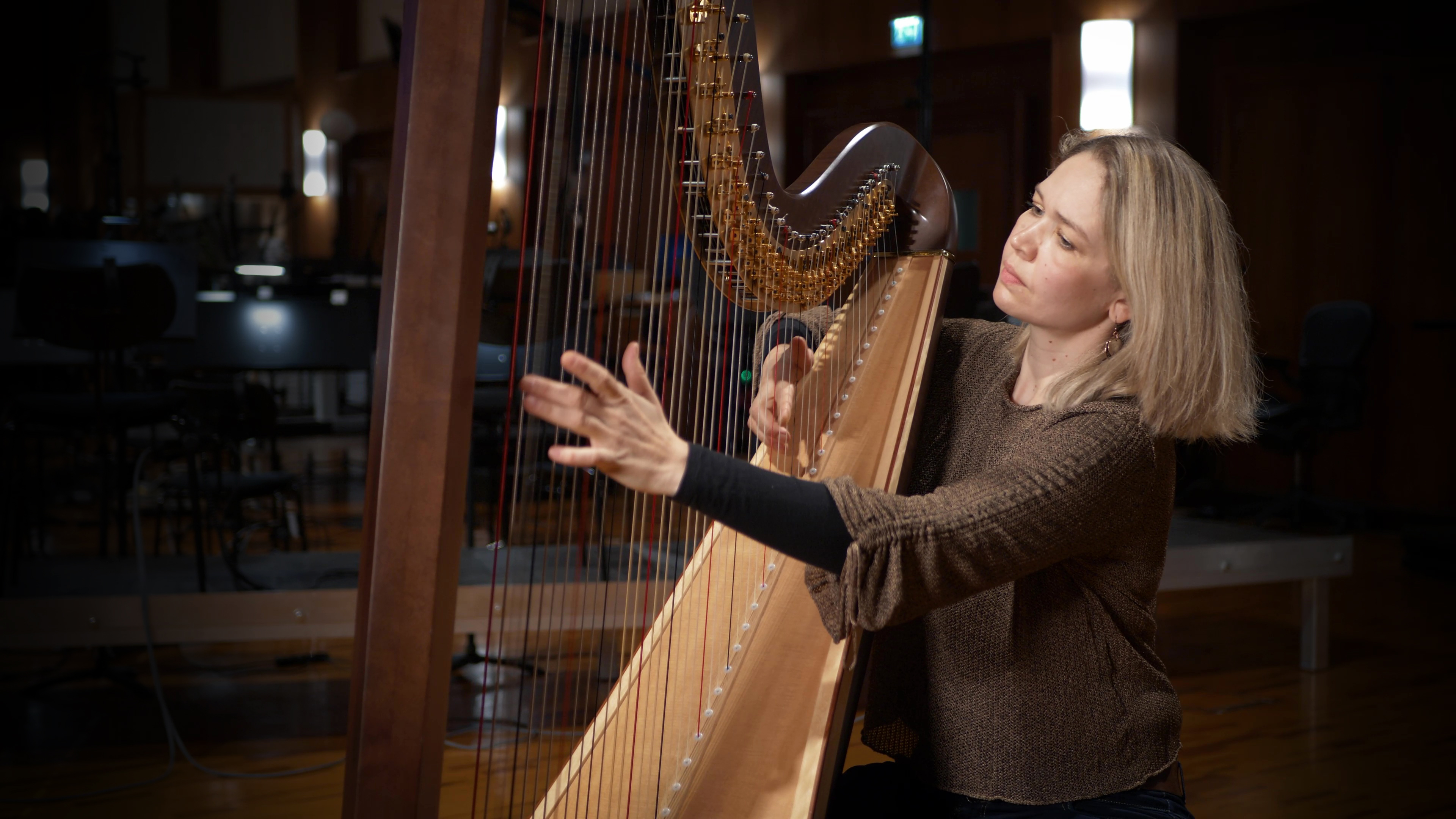 blonde woman playing a harp in a dark music studio with instruments visible