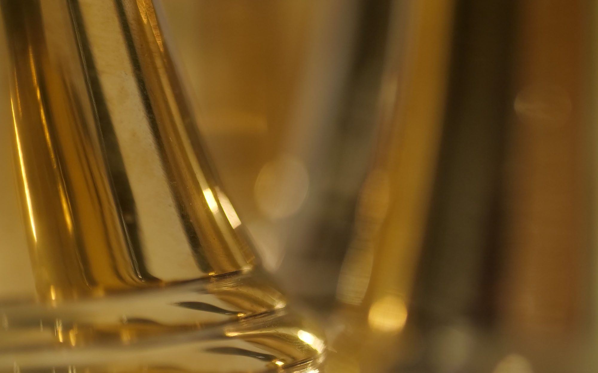 Abstract close-up of a reflective, golden-toned surface with blurred light reflections and vertical lines, suggesting glass or polished metal.
