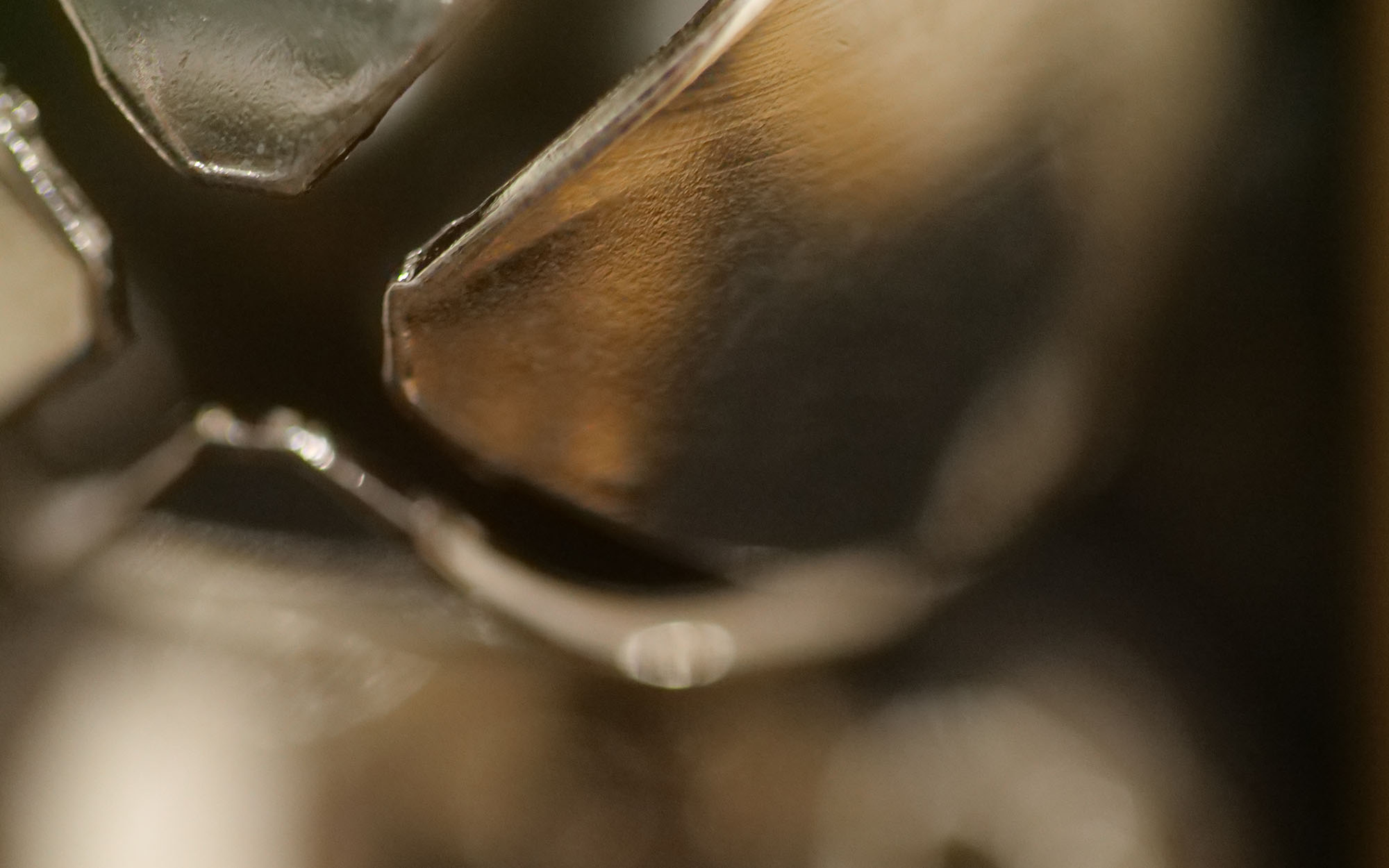 Macro close-up of a textured metallic surface with reflective highlights and shadow details, showing an abstract pattern