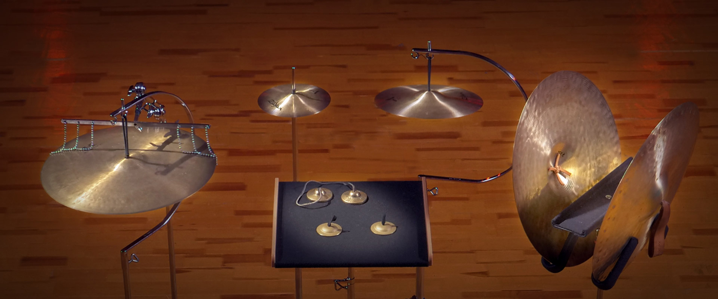 Percussion setup with various cymbals, including suspended, crash, splash, and finger cymbals, arranged on stands over a wooden floor.