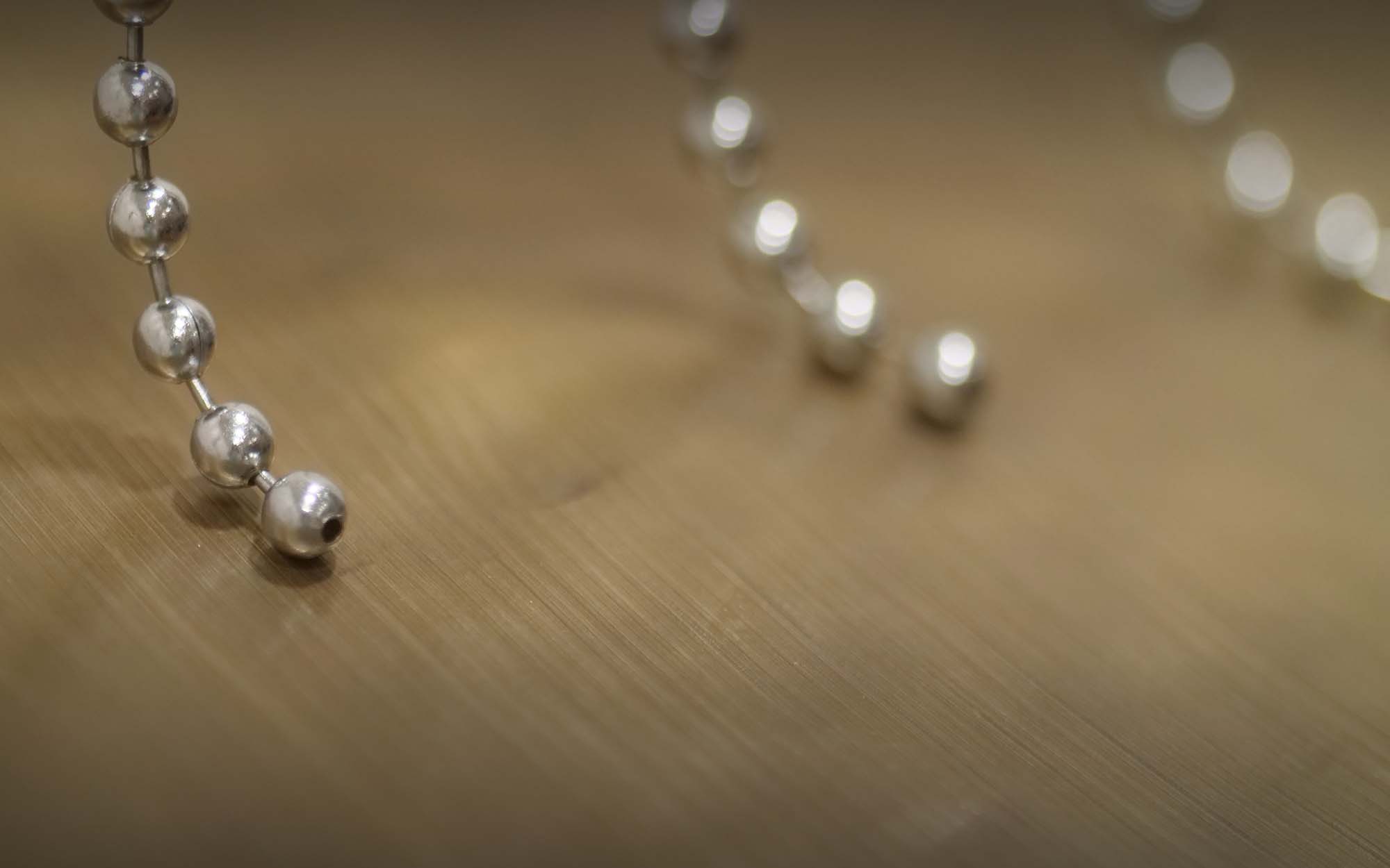 Close-up of a silver beaded chain from window blinds, with a wooden surface in the background and a shallow depth of field.