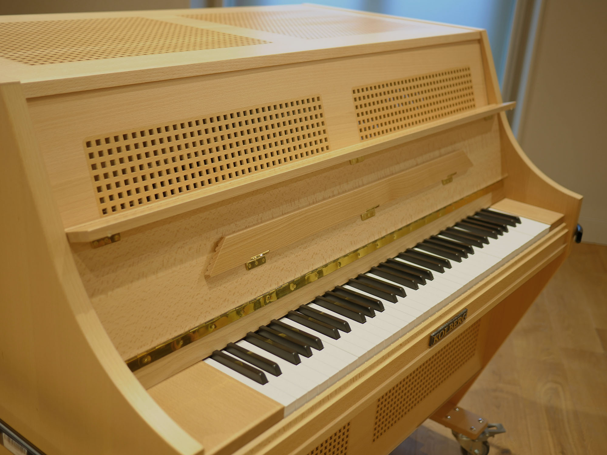 Light wood Kolberg celesta with black and white keys, brass hinges, and perforated accents, angled view showing the keyboard and the instrument’s side.