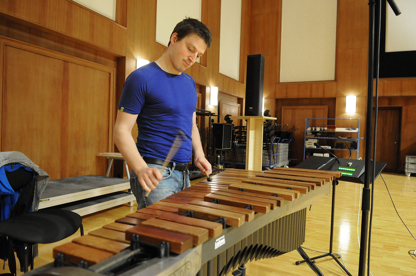 Man playing a marimba percussion instrument with mallets in a music studio or concert hall.