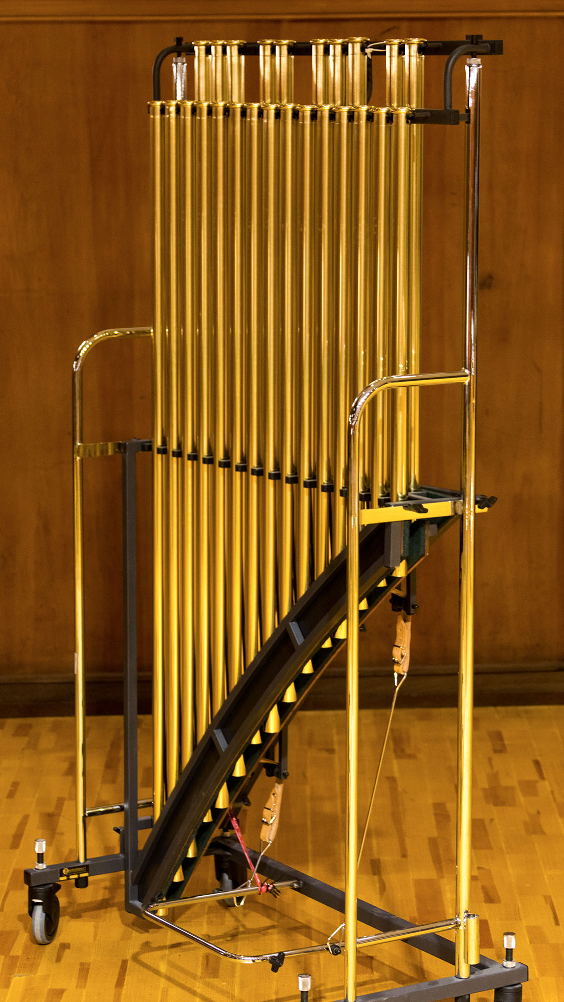 Orchestral chimes instrument, gold-colored tubular bells on a black and chrome rolling stand, with wooden mallets visible.